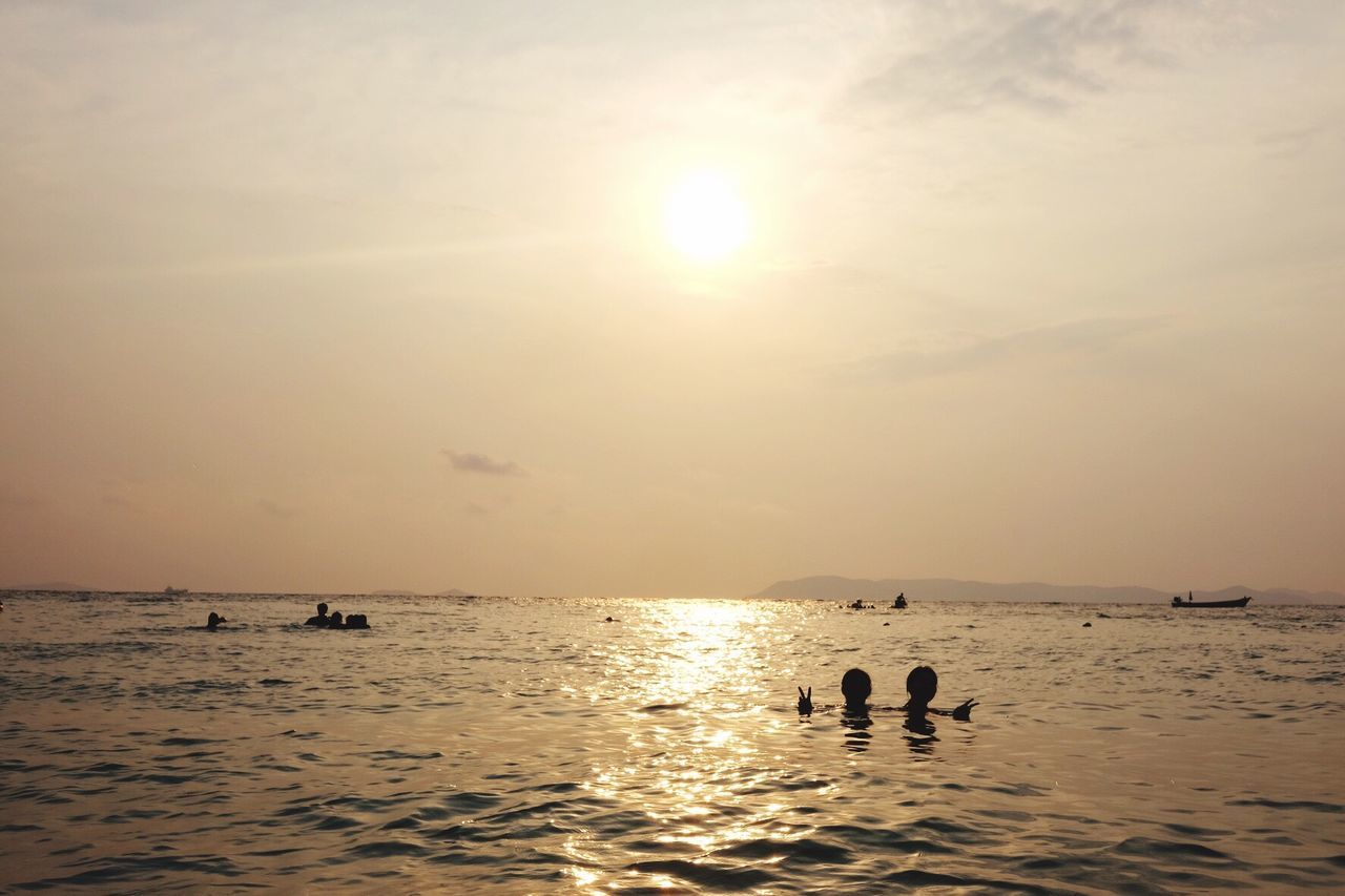 Sun shining over sea with people swimming