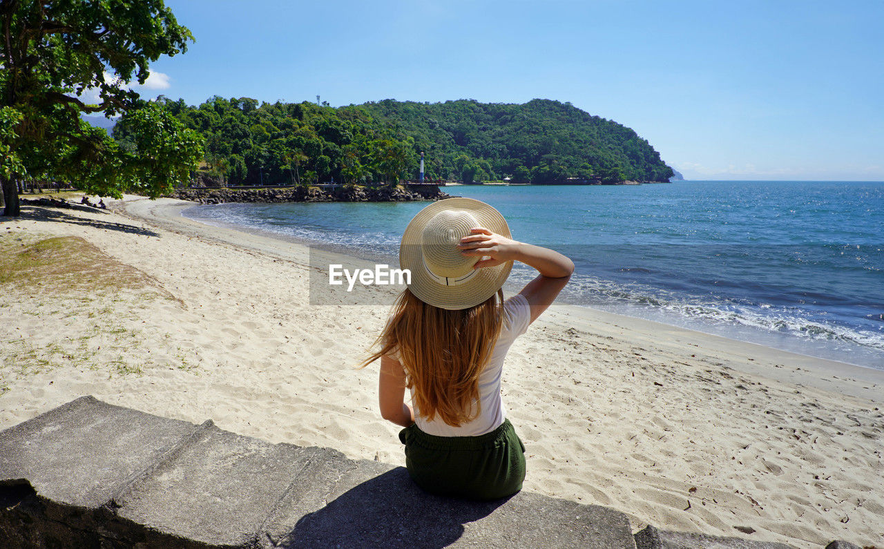 Holidays in brazil. back view of traveler girl sitting on wall in ubatuba beach, brazil.