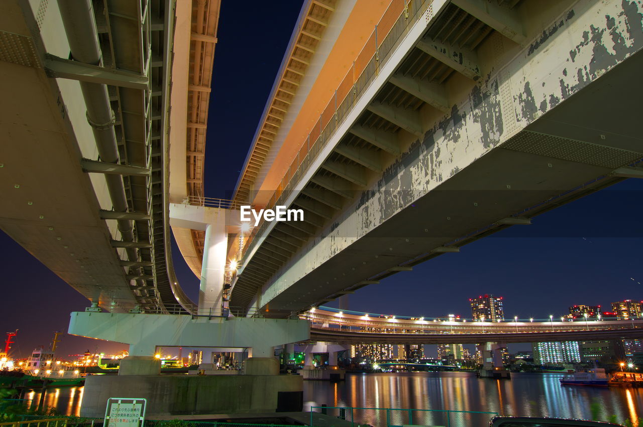LOW ANGLE VIEW OF ILLUMINATED BRIDGE OVER RIVER IN CITY