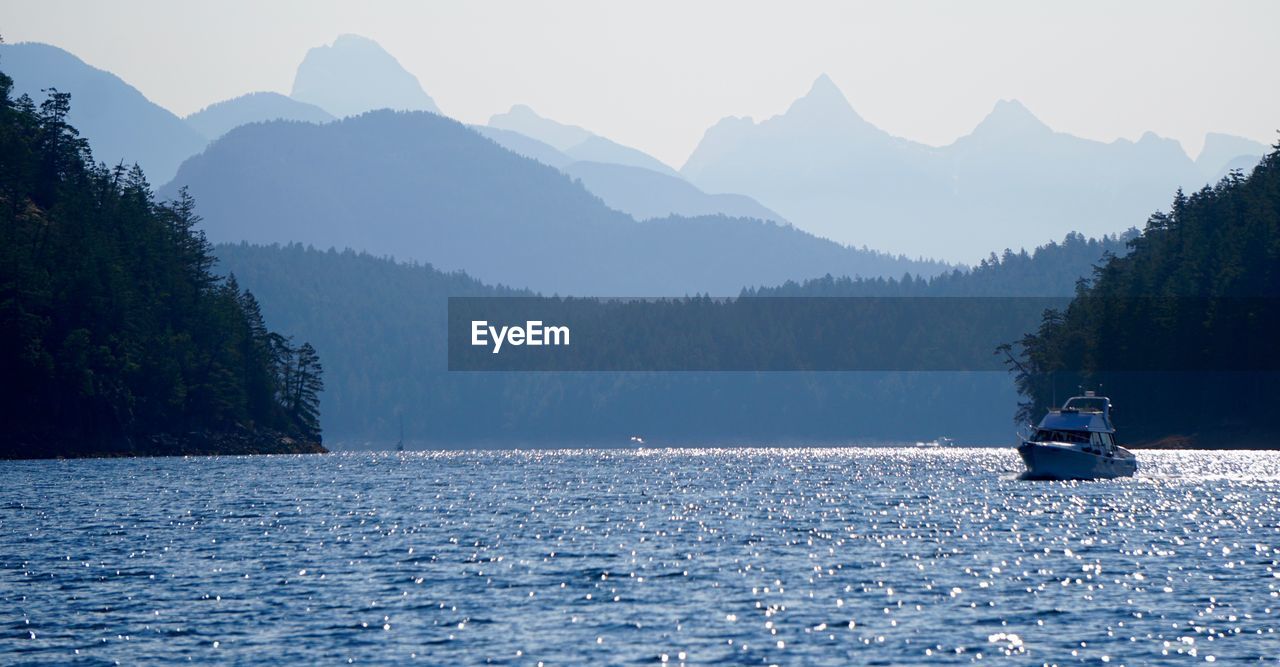 Boat sailing on lake by mountains against clear sky