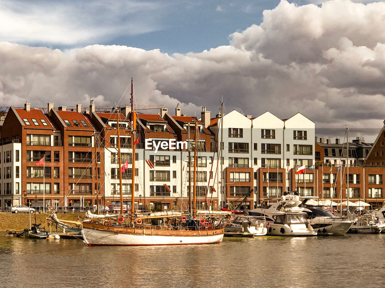 Sailboats moored on river by buildings against sky