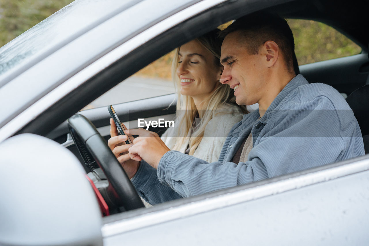 A young couple on a road trip looking at a map on their phone in a navigator.