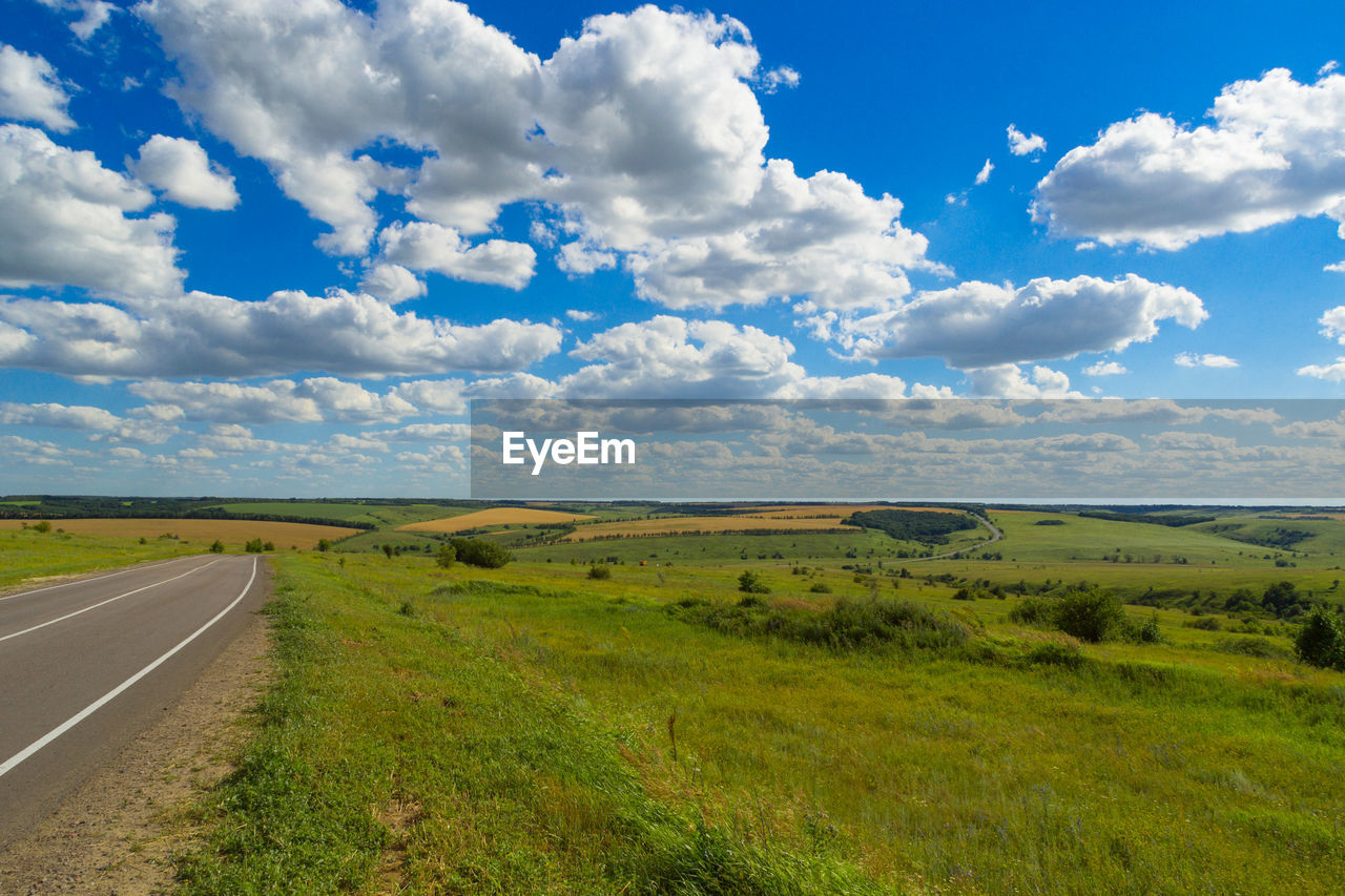 Empty road by grassy landscape against sky