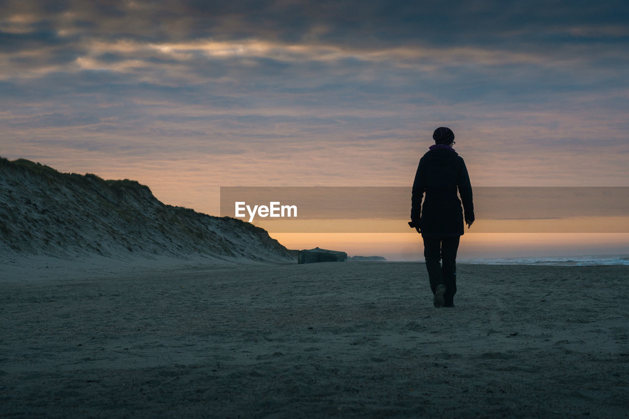 Rear view of woman walking at beach against sky