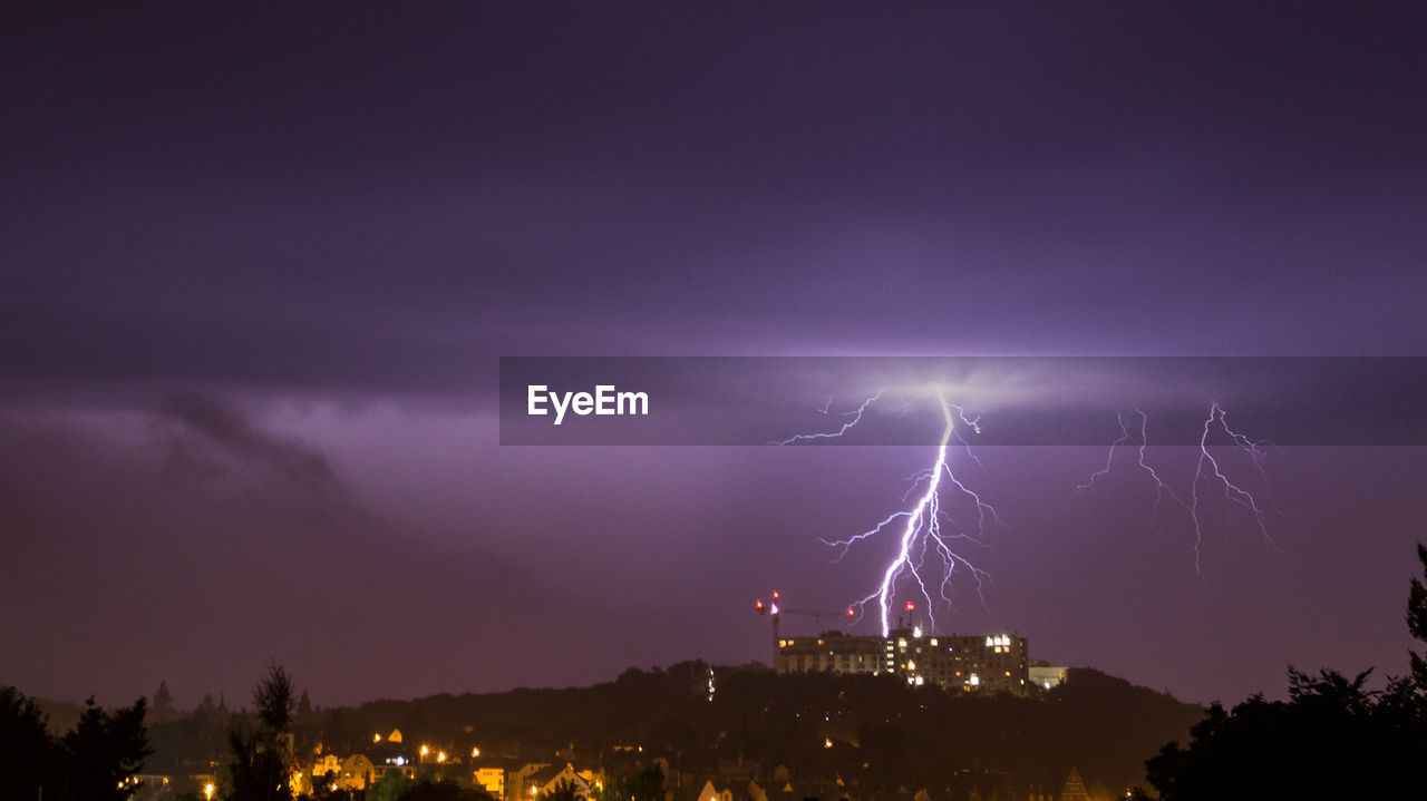 Lightning over illuminated cityscape against sky at night