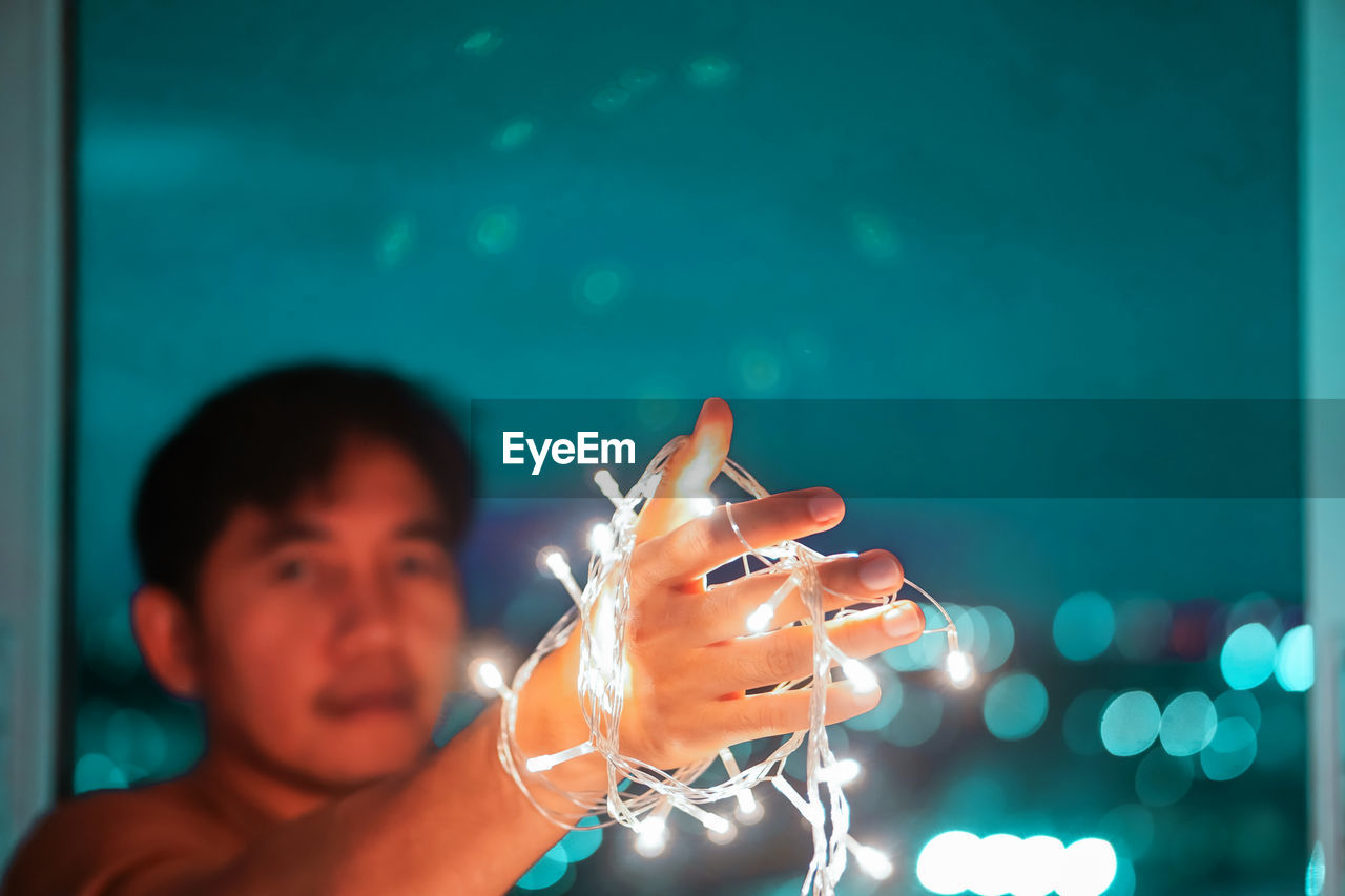 CLOSE-UP PORTRAIT OF MAN HOLDING ILLUMINATED LIGHT