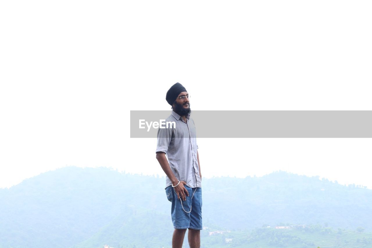 Young man wearing turban looking away against clear sky