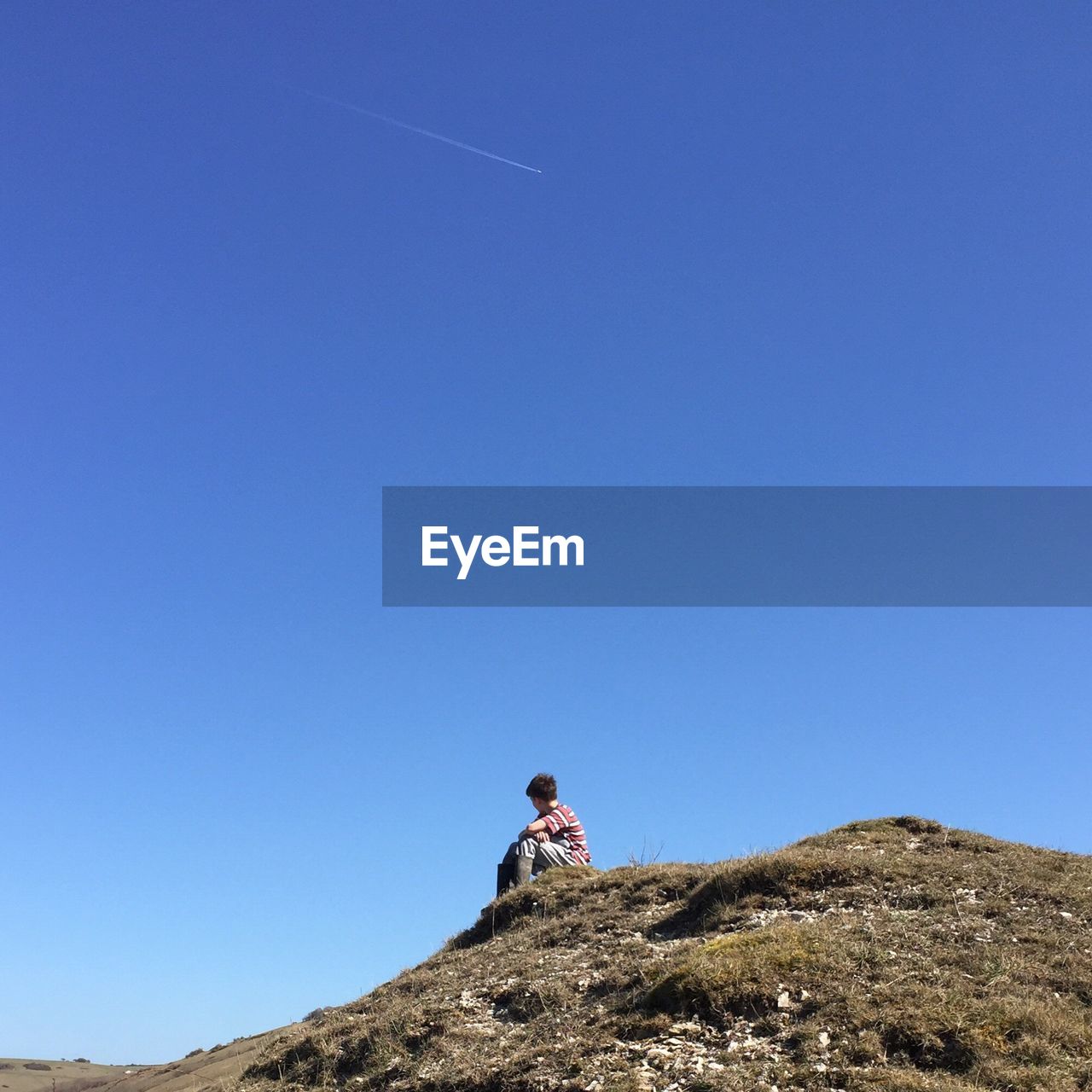 Low angle view of boy sitting on hill against clear sky