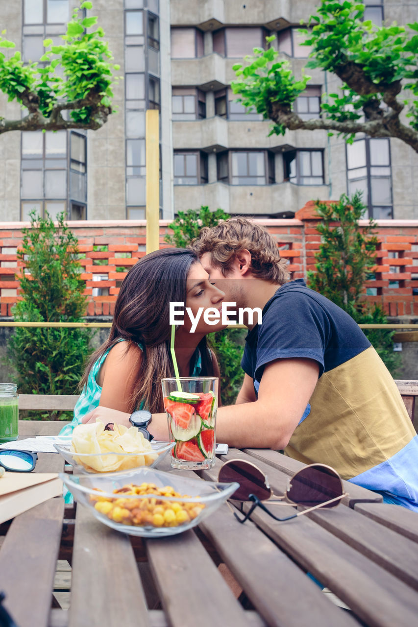 Man whispering in woman ear by food and drink at restaurant