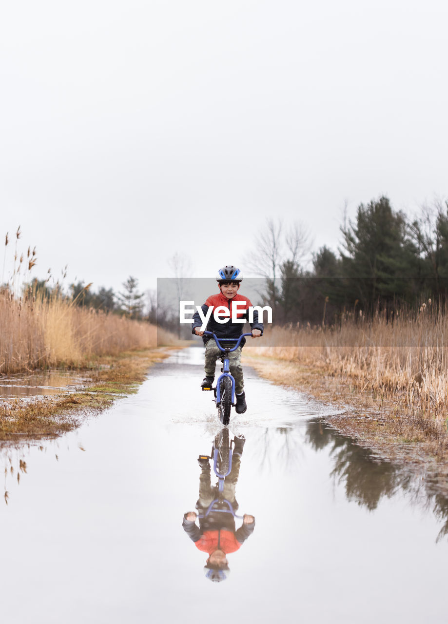 Young boy riding his bike through a puddle on a flooded trail.