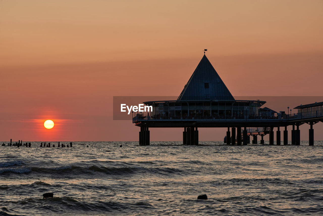 sunset, water, sky, sea, architecture, ocean, horizon, built structure, evening, nature, dawn, beauty in nature, beach, coast, building exterior, land, building, wave, travel destinations, shore, scenics - nature, sun, tower, travel, horizon over water, tranquility, orange color, no people, religion, pier, motion, idyllic, silhouette, outdoors, environment, dramatic sky, tranquil scene, cloud, twilight, landscape, tourism, afterglow, romantic sky, seascape, sunlight, reflection, transportation