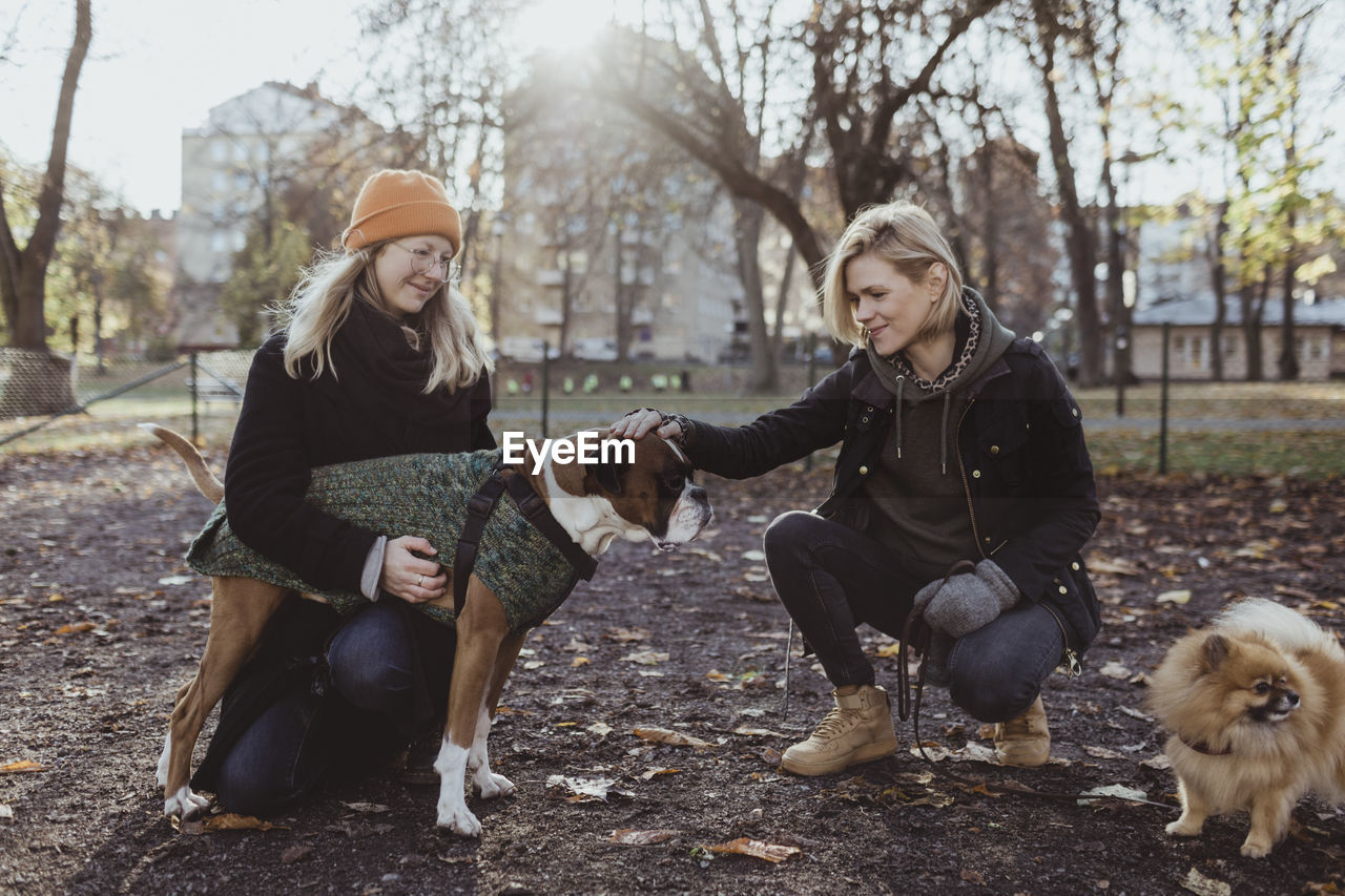 Women crouching while stroking boxer dog at park during autumn