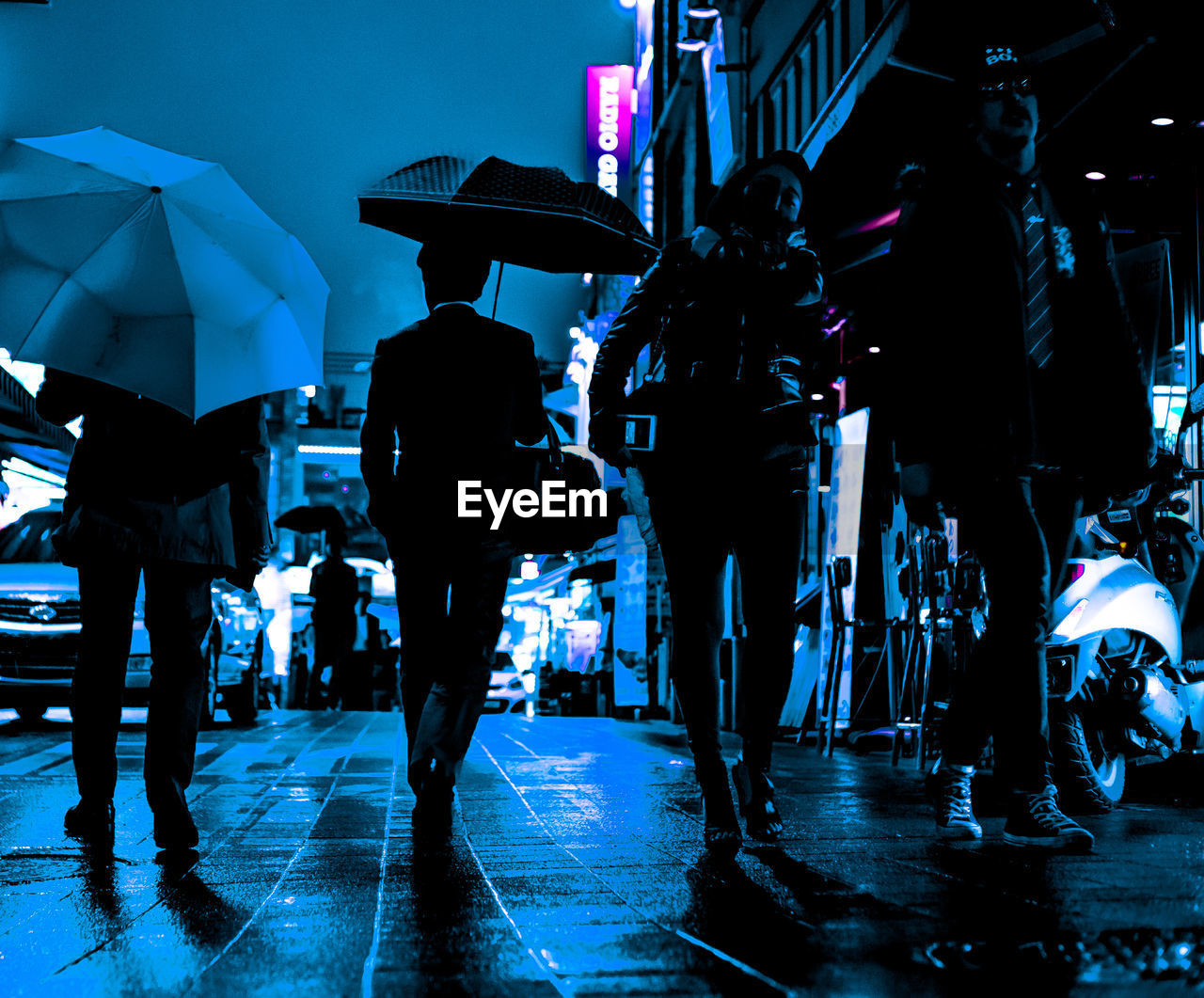 PEOPLE WALKING ON WET ILLUMINATED STREET DURING RAINY SEASON