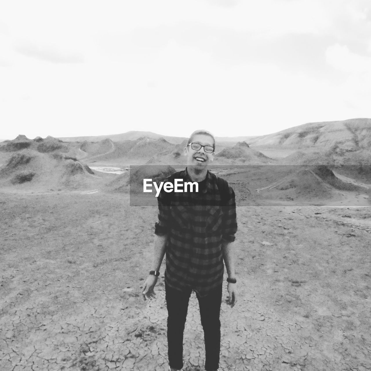 Cheerful young man standing by mud volcanoes against sky