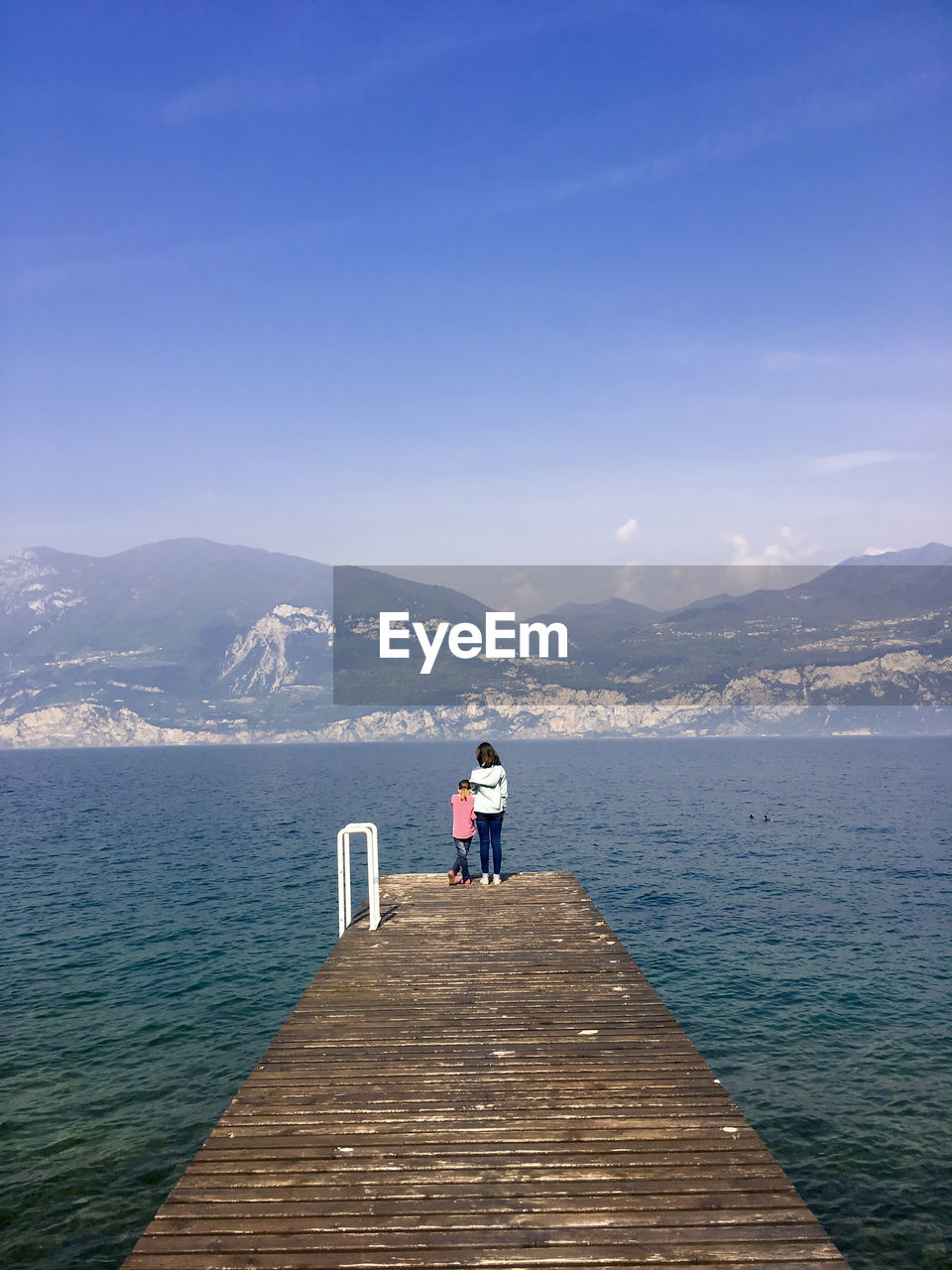 Rear view of siblings on pier over lake against sky