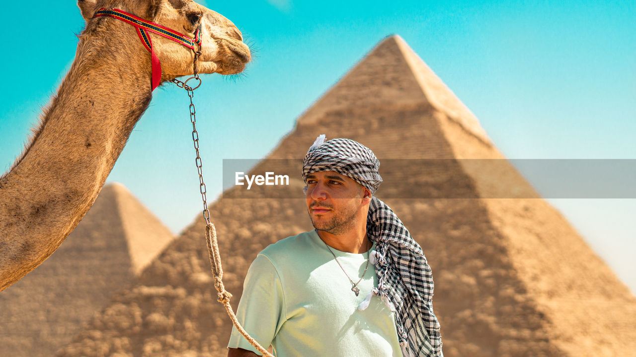 Full length of a man standing on sand at desert with the pyramids behind