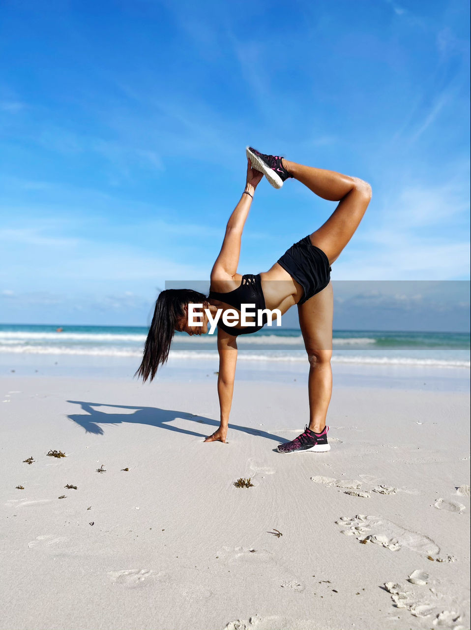 full length of woman doing yoga at beach against sky