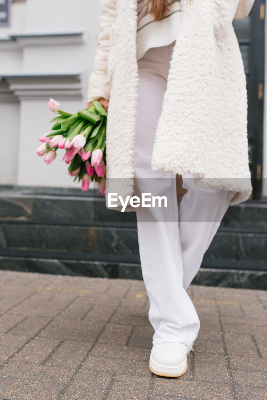 Bouquet of tulips in a woman's hand and white pants in red close-up