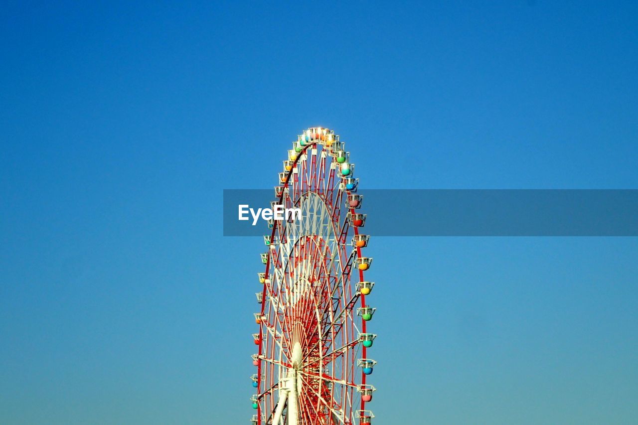 Low angle view of ferris wheel against clear blue sky