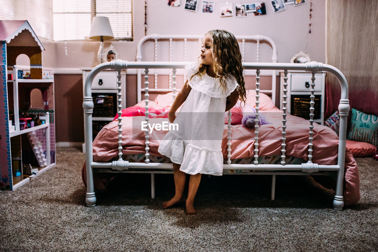 Young girl standing at the end of her bed looking away