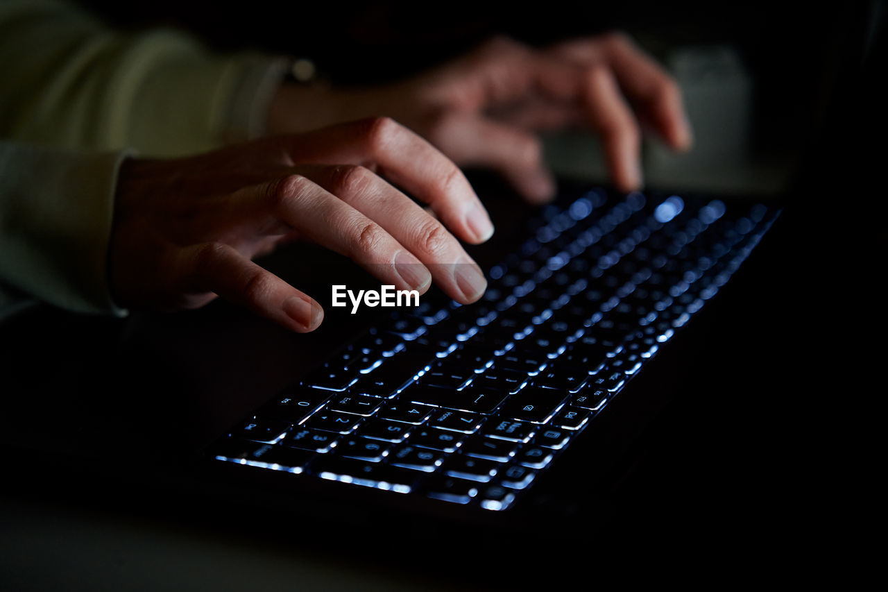 Typing on laptop keyboard at night, close up