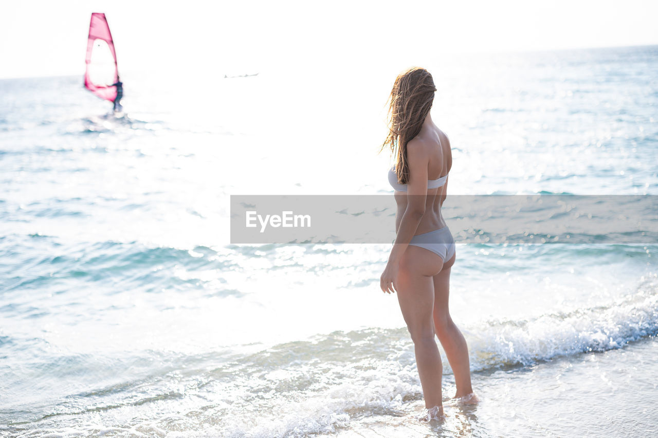 Full length of woman in bikini standing on beach against sky