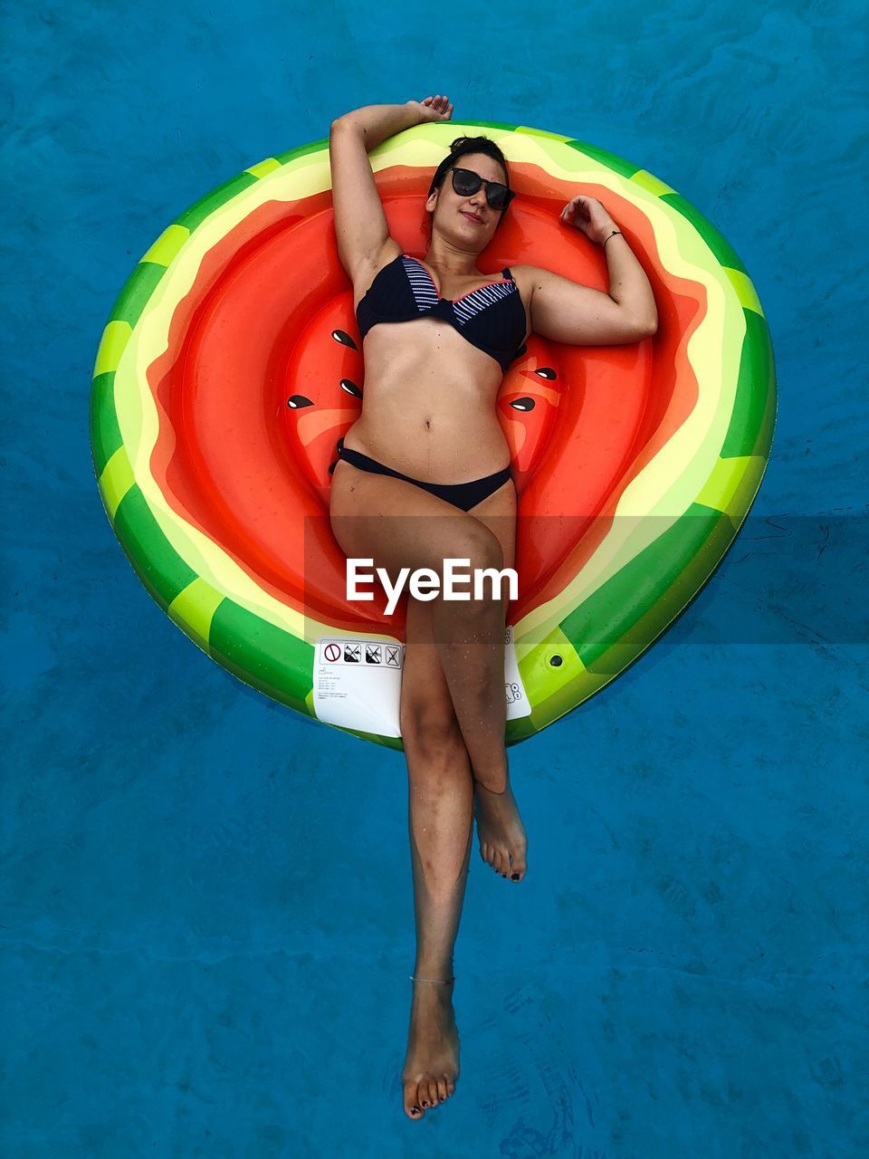 High angle view of teenage girl wearing bikini lying on inflatable raft in swimming pool