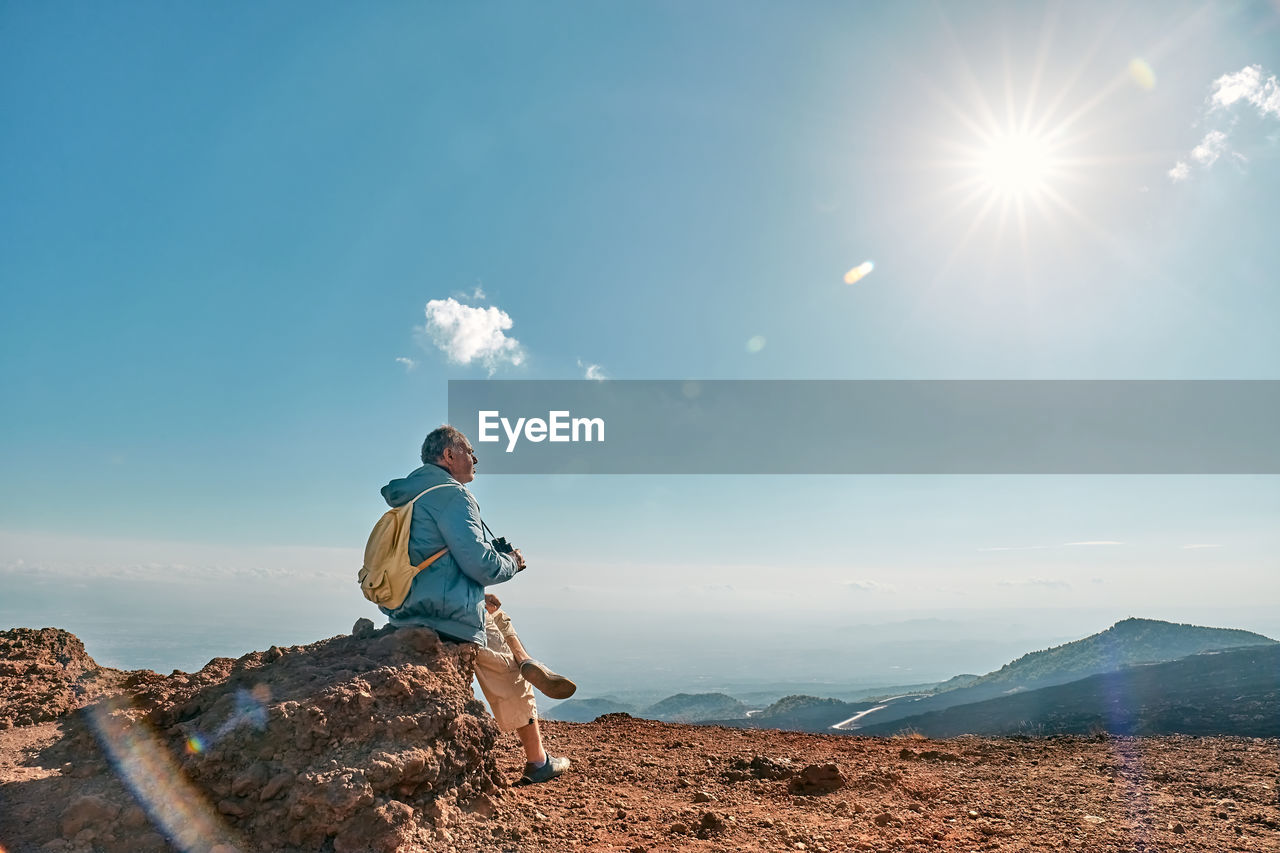 Rear view of man looking through binoculars at panoramic view of colorful summits of volcano etna.