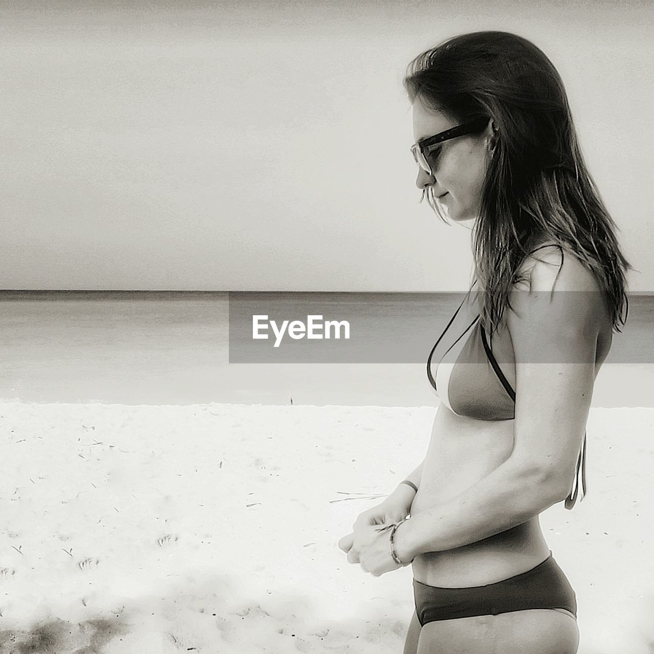 Side view of woman wearing bikini standing at beach against sky