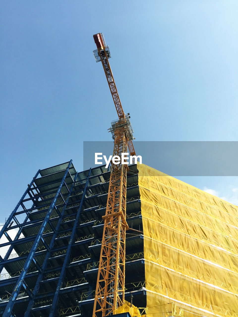 Low angle view of crane on building against clear sky during sunny day