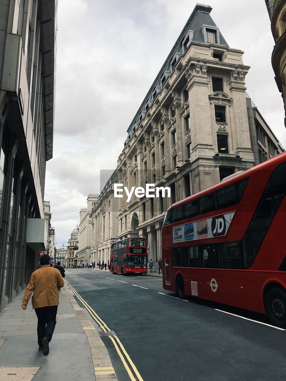 REAR VIEW OF MAN WALKING ON STREET AMIDST BUILDINGS