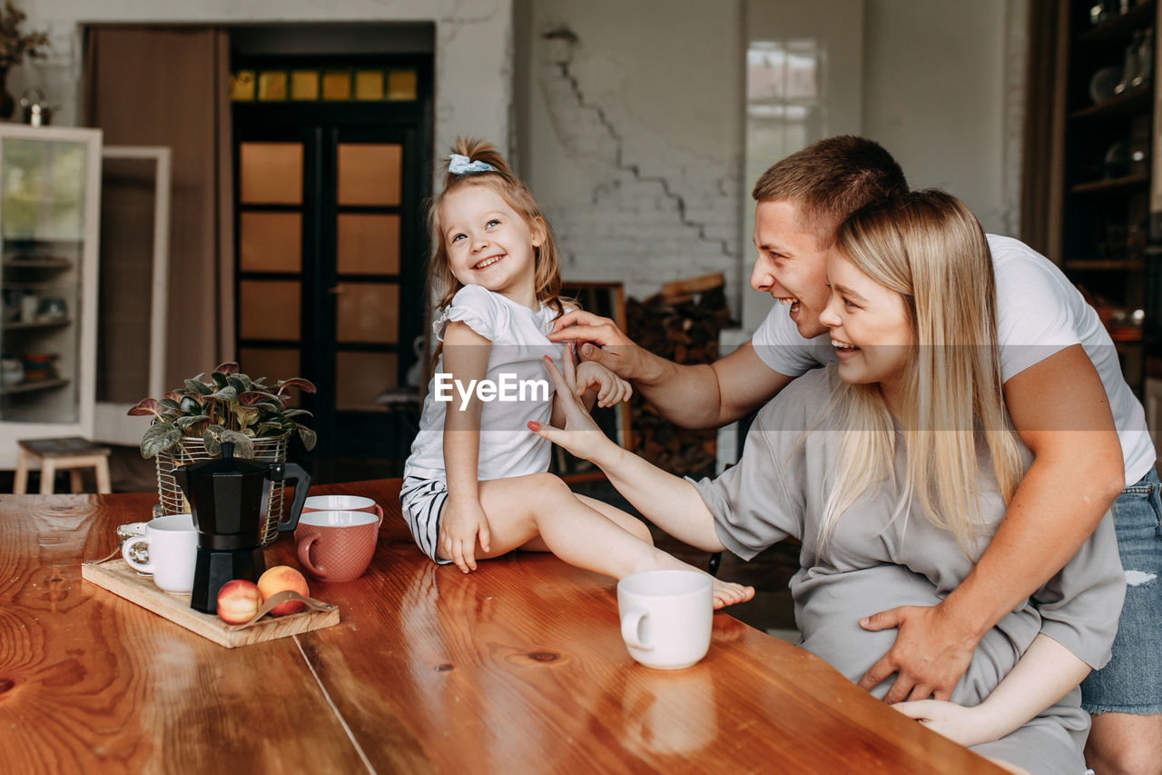 A family with a child having breakfast drinking tea laughing and having fun in the kitchen at home