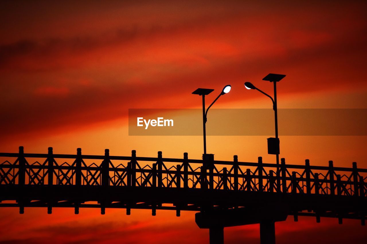 Silhouette of pier on sea against orange sky