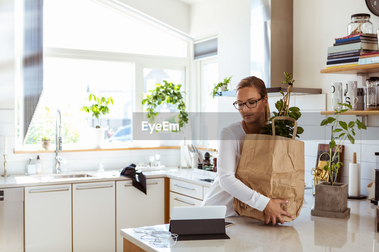 Woman holding paper bag while looking at digital tablet in kitchen