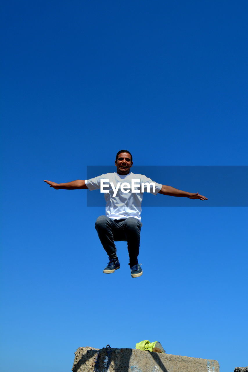 LOW ANGLE VIEW OF MAN JUMPING AGAINST CLEAR SKY