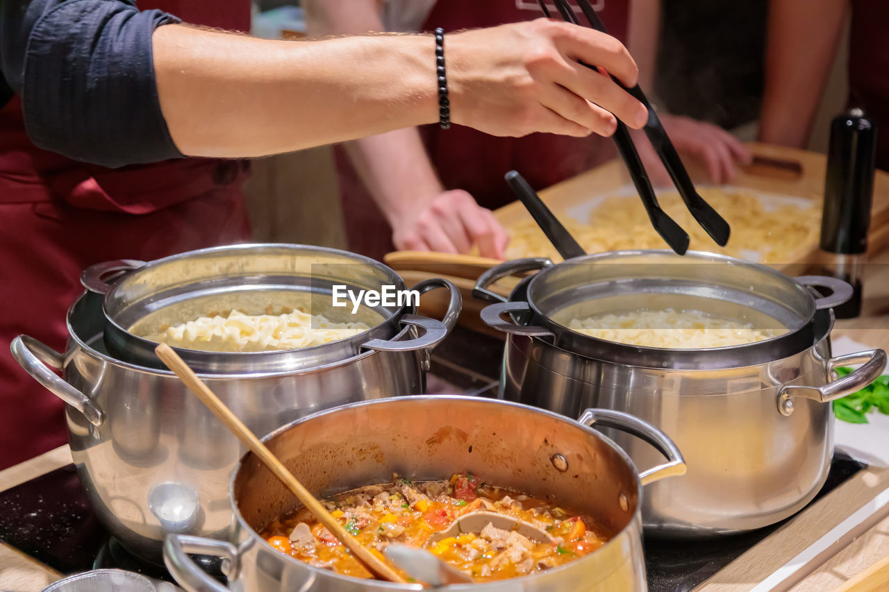 The chef prepares pasta in large metal pans. male hands take out the pasta from the pan with tongs.