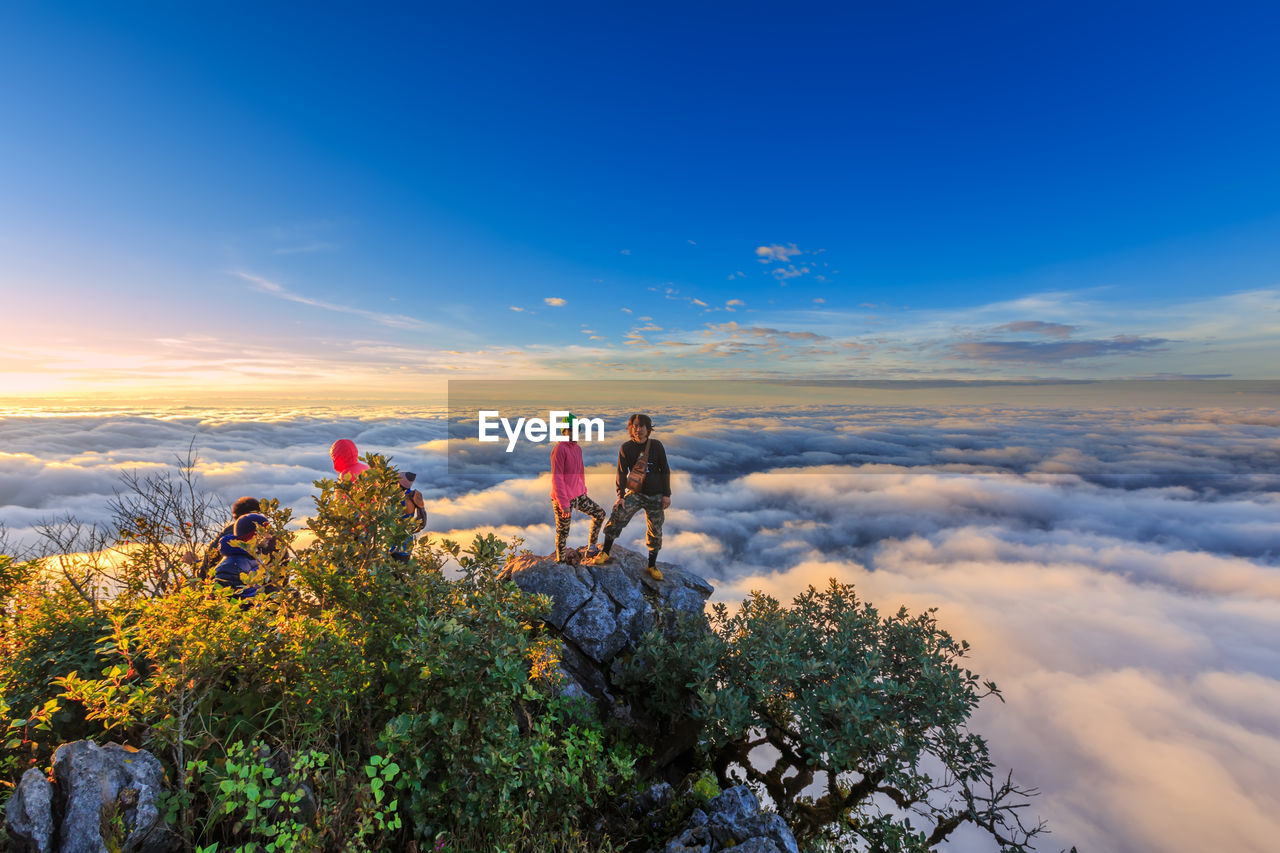 MEN STANDING ON ROCK AGAINST SKY DURING SUNSET