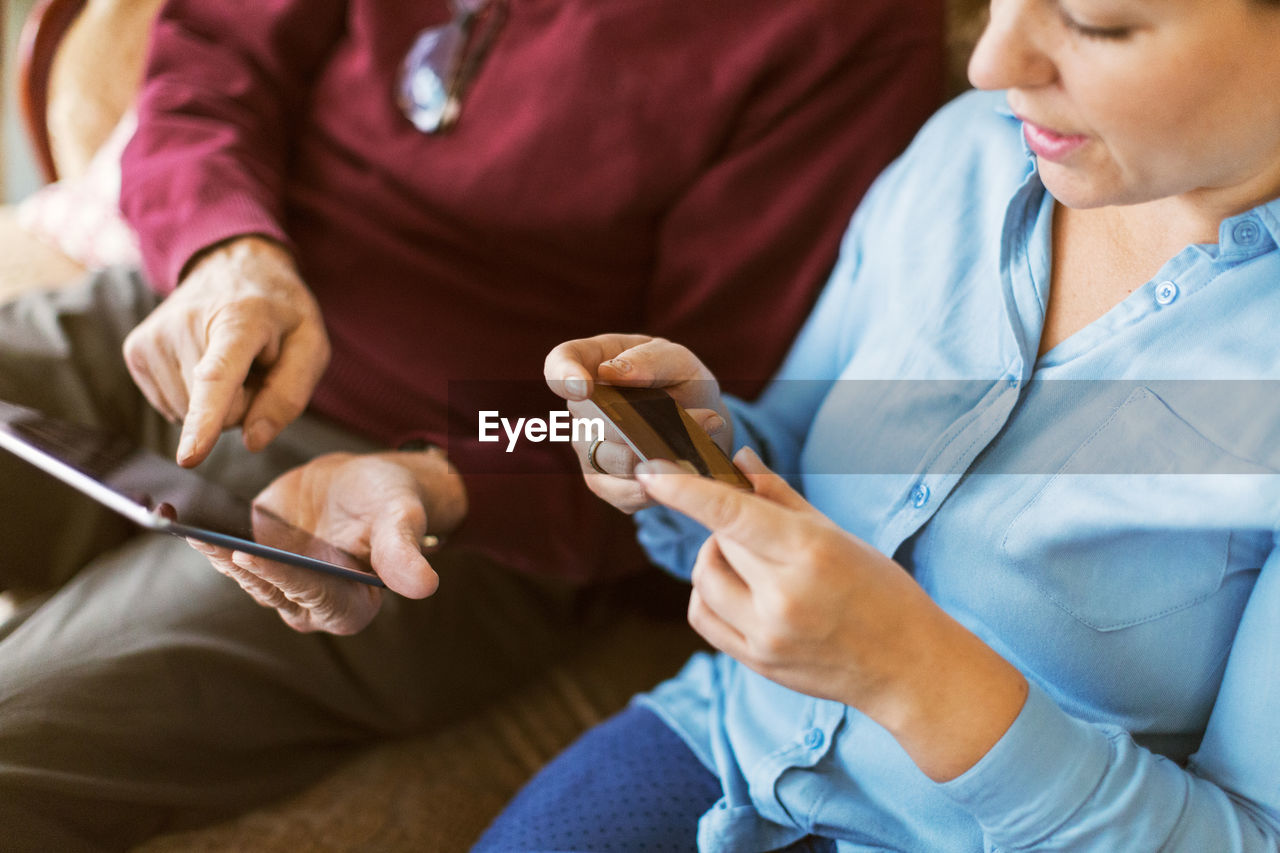 High angle view of senior man doing online shopping with daughter through credit card and digital tablet