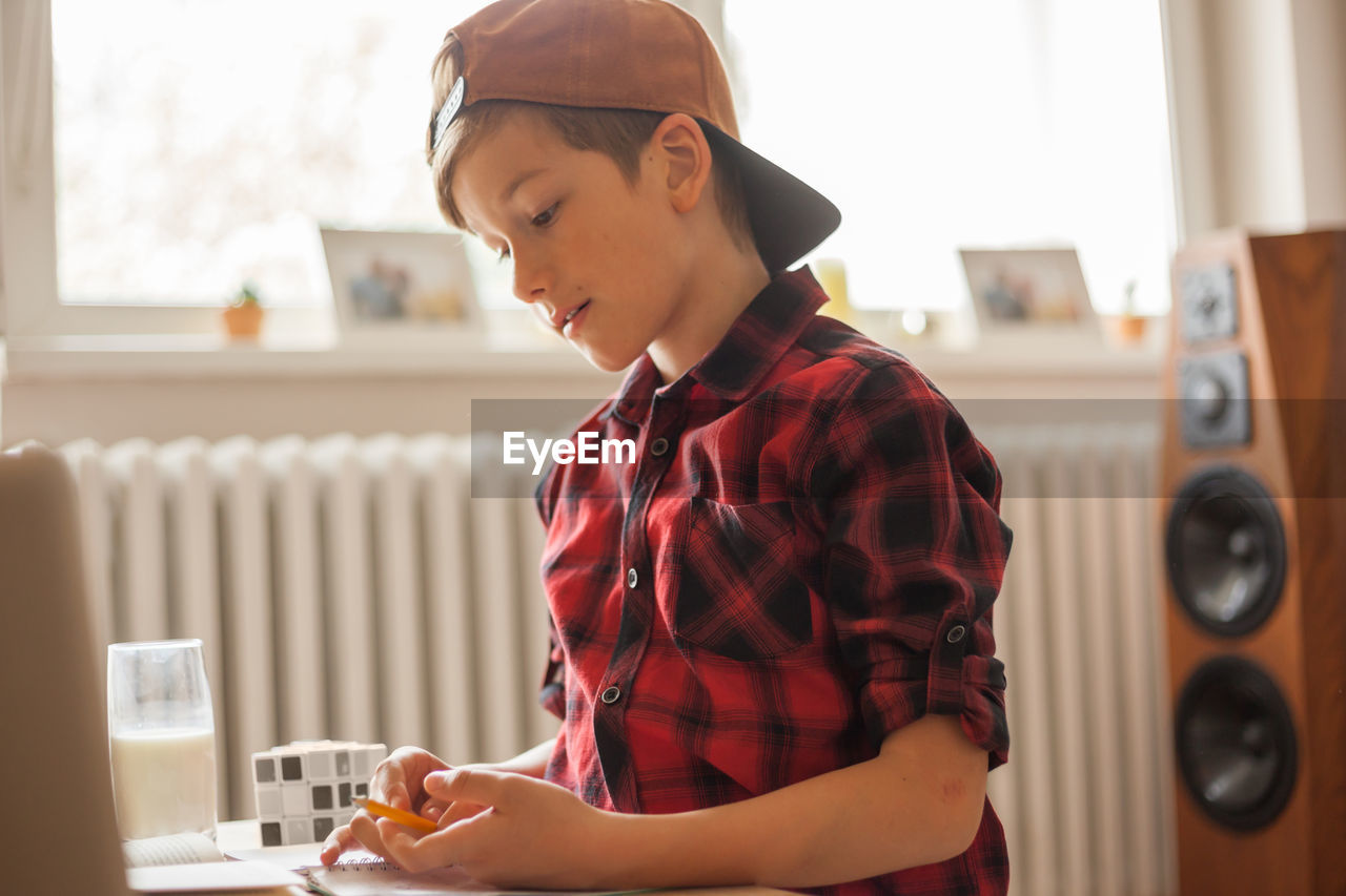 Cute boy with a cap studying at home due to coronavirus epidemic.