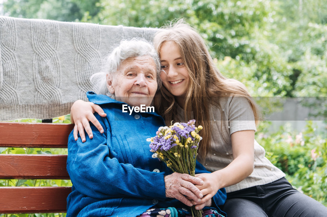 Volunteer girl and senior elderly woman with gift, flowers bouquet and basket of groceries