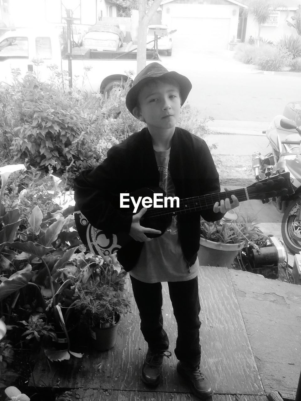 Portrait of boy holding guitar while standing on sidewalk