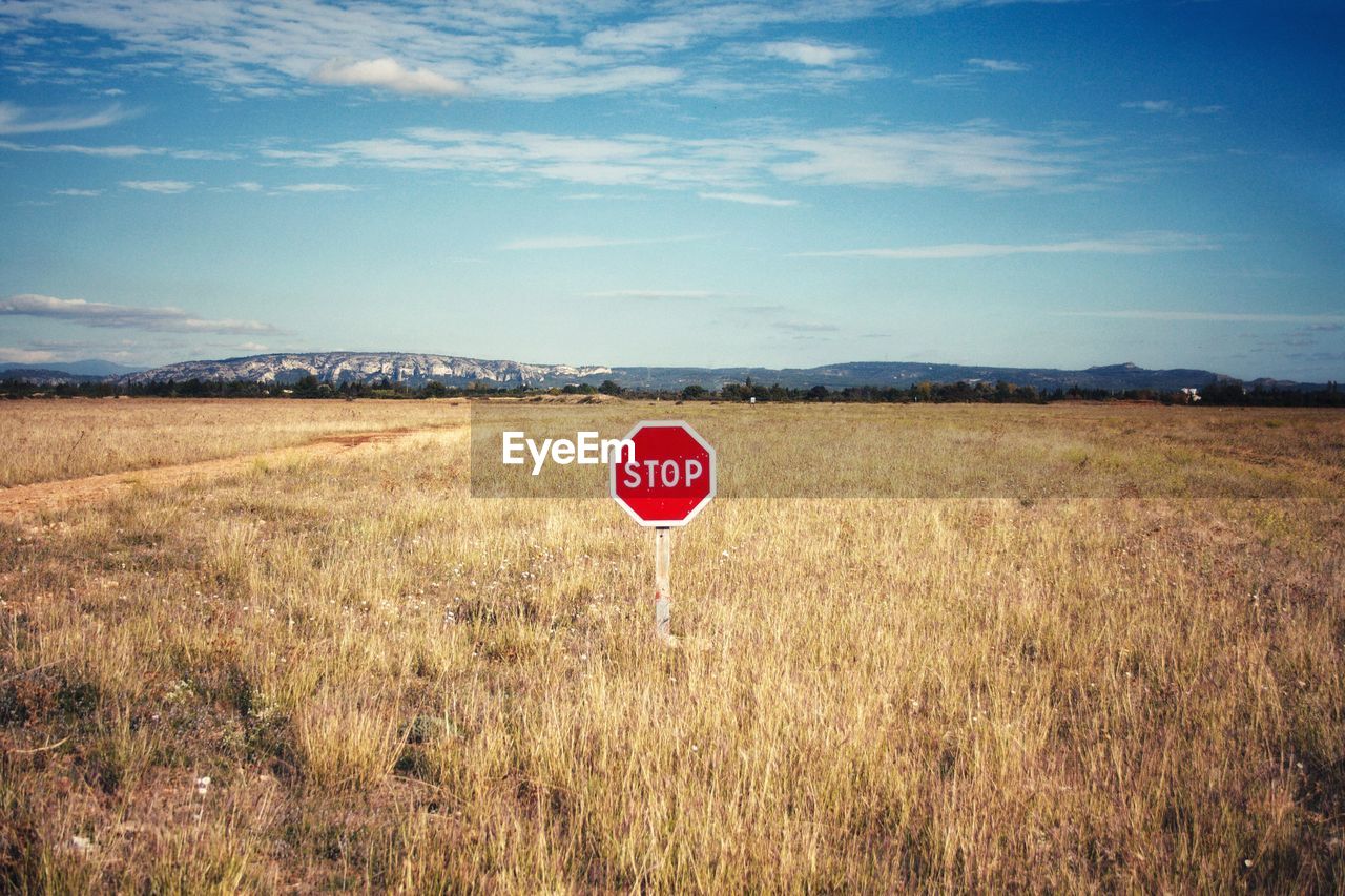 Stop sign on grassy field against sky