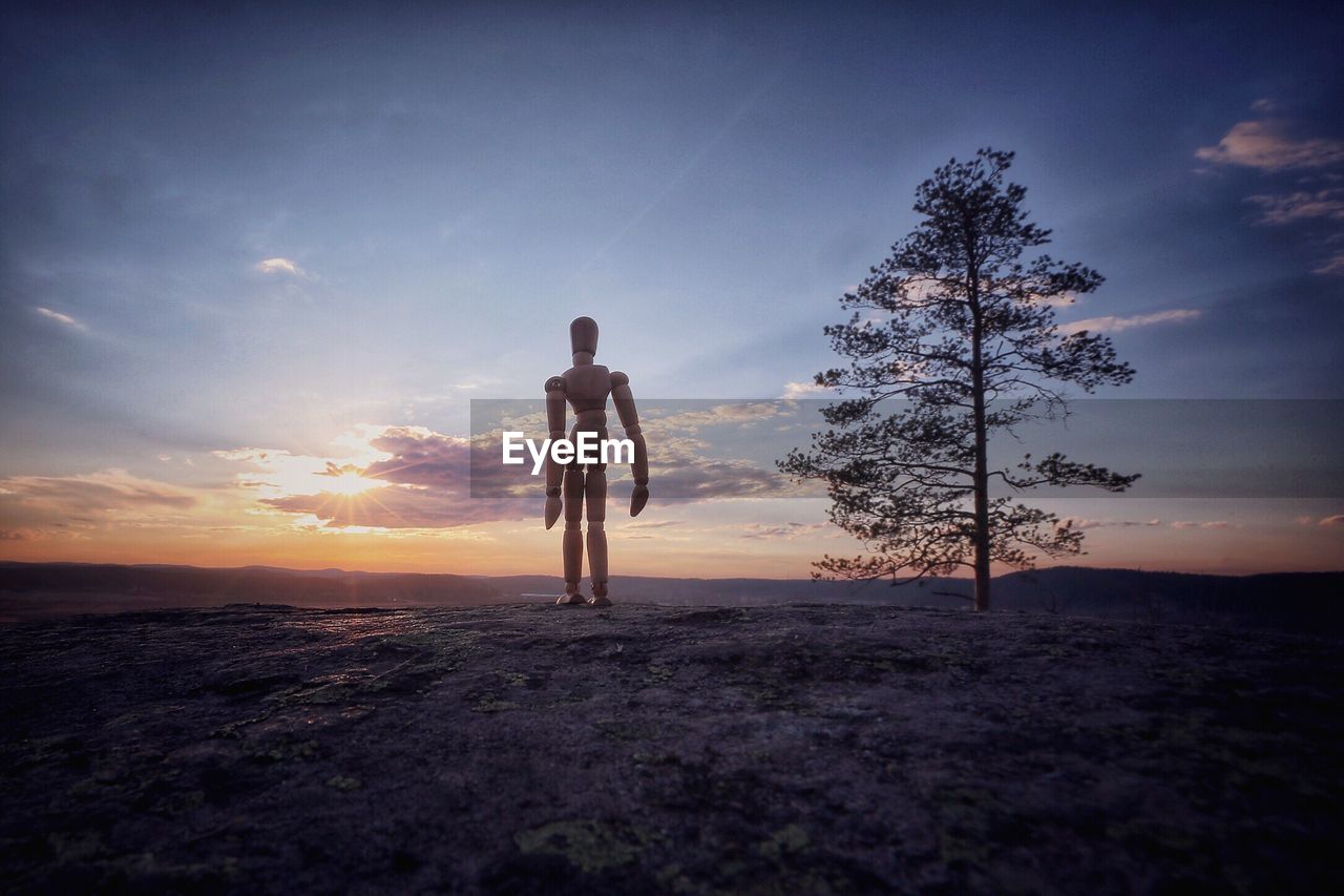 Wooden mannequin standing on landscape during sunset