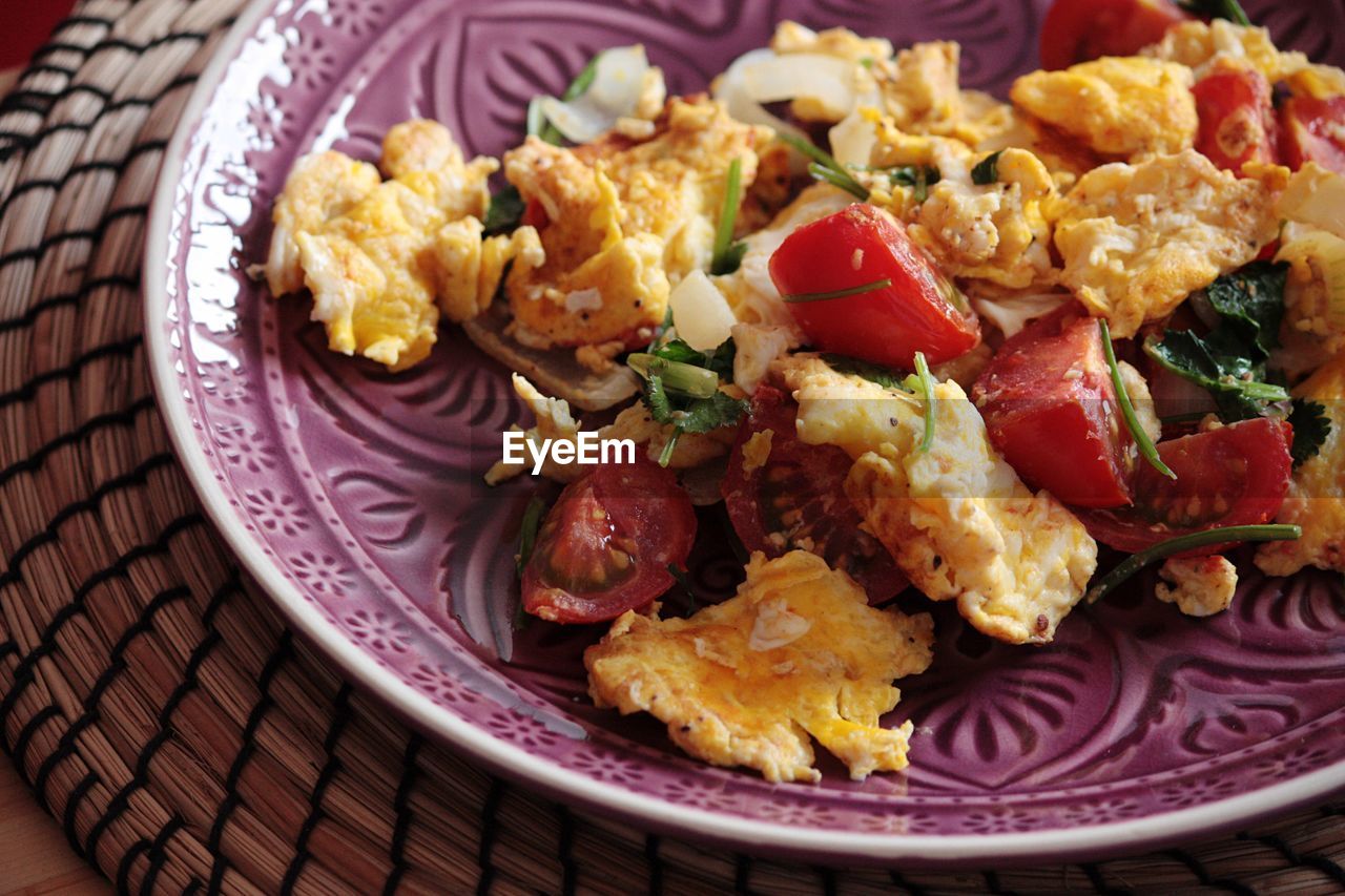 High angle view of scrambled eggs with tomatoes in plate on mat