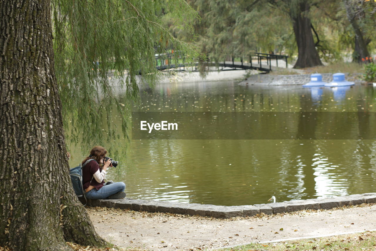 Side view of man sitting on tree trunk by lake