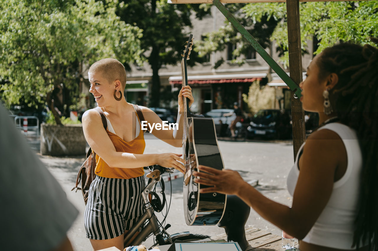 Smiling woman looking away holding guitar at flea market