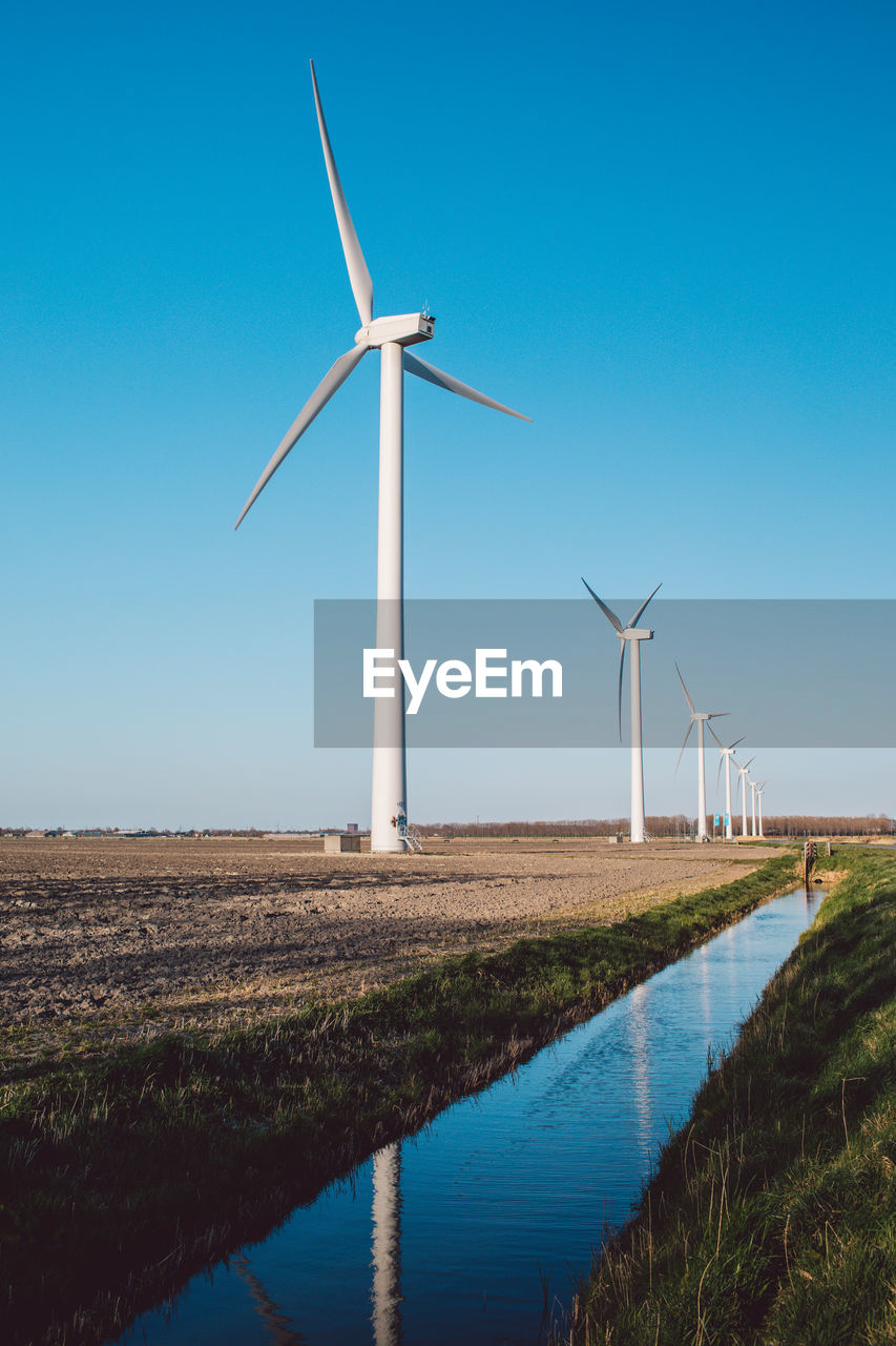 Windmill on field against clear blue sky