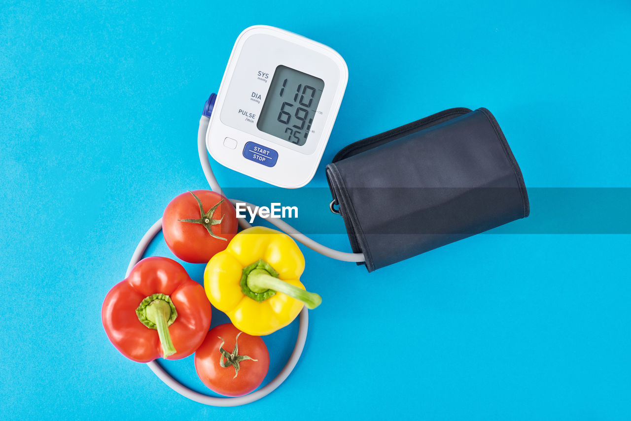 Digital blood pressure monitor and fresh vegetables on blue background. healthcare concept