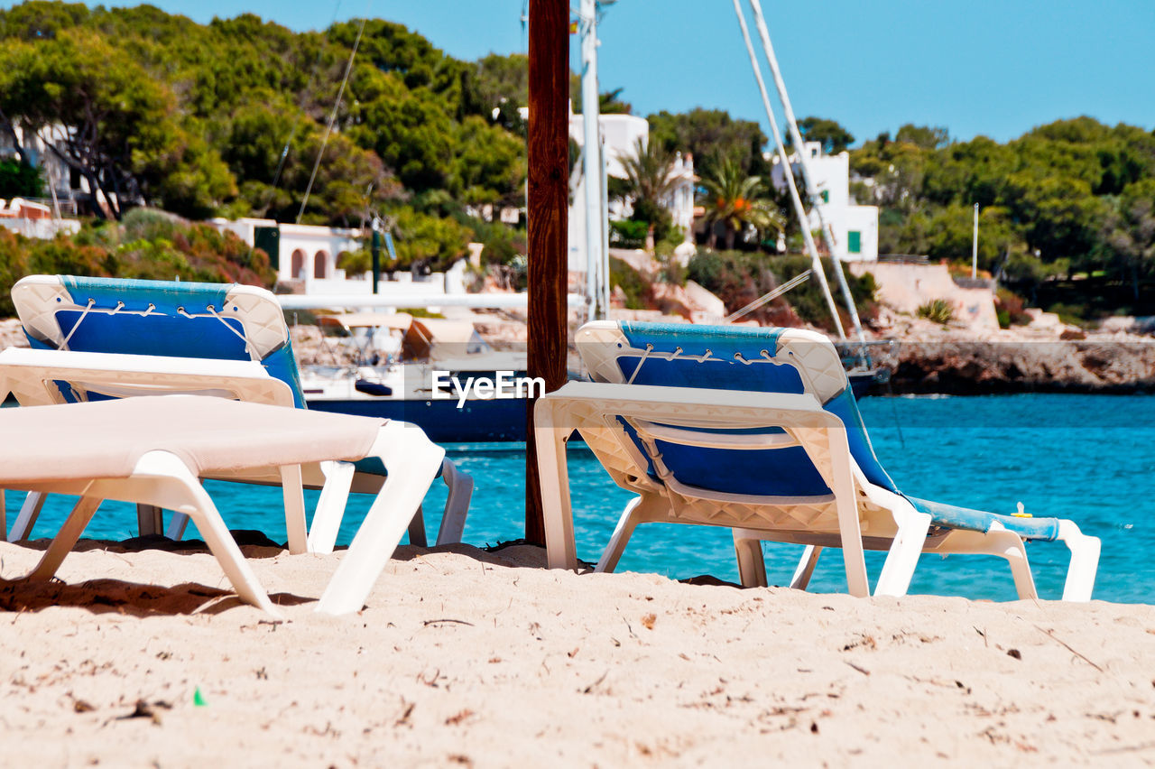 Deck chairs on beach against sky