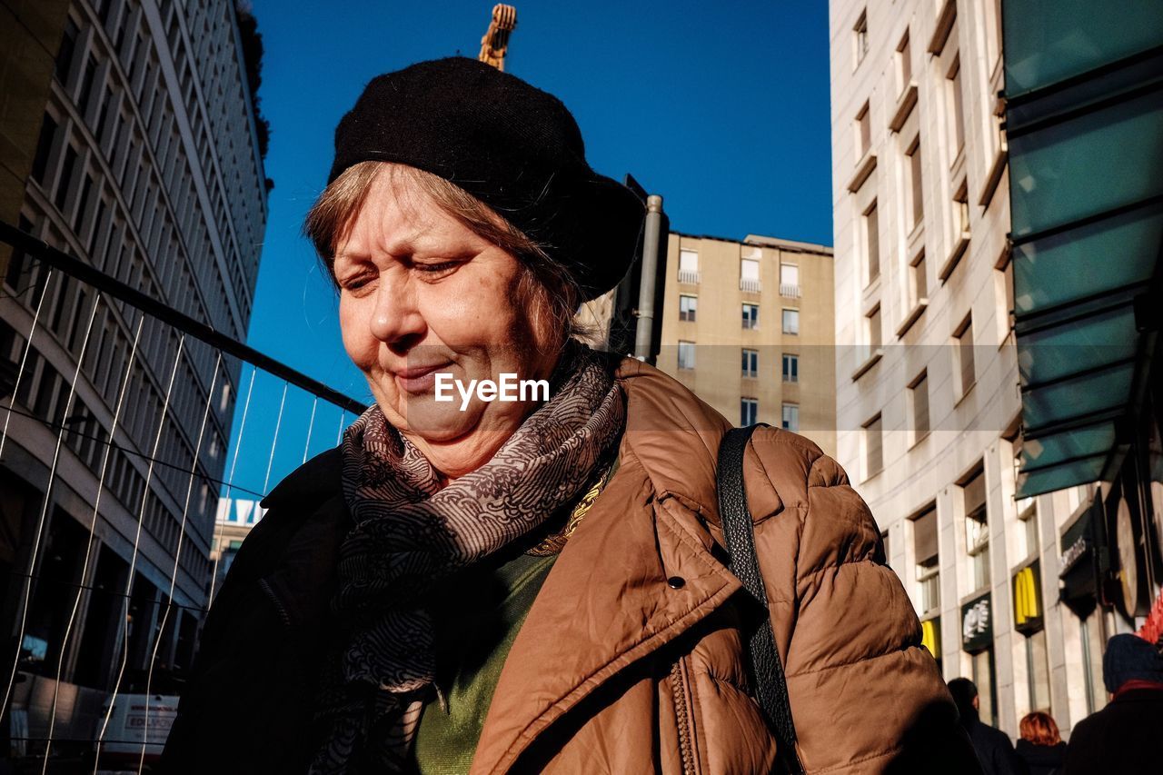 LOW ANGLE PORTRAIT OF MAN STANDING AGAINST BUILDINGS